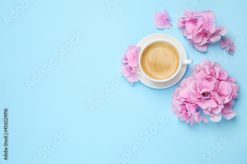 Beautiful hortensia flowers and coffee on light blue background, flat lay. Space for text