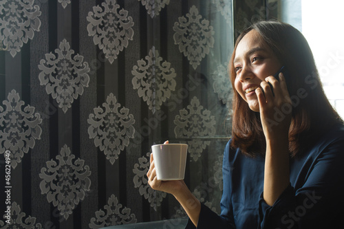 Relaxed Smilling Asian Woman drinking coffee while using a cell phone for work