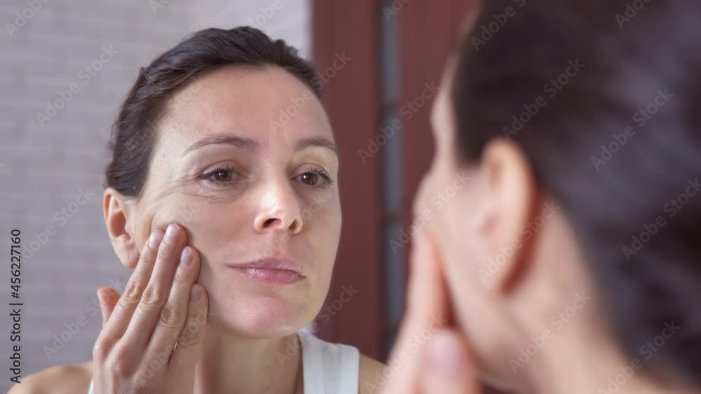 Woman touching face in the mirror. A woman look at her skin with wrinkes in the mirror in the room. Woman touching face in the mirror. A woman look at her skin with wrinkes in the mirror in the room.