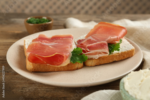 Delicious sandwiches with cream cheese and jamon on wooden table