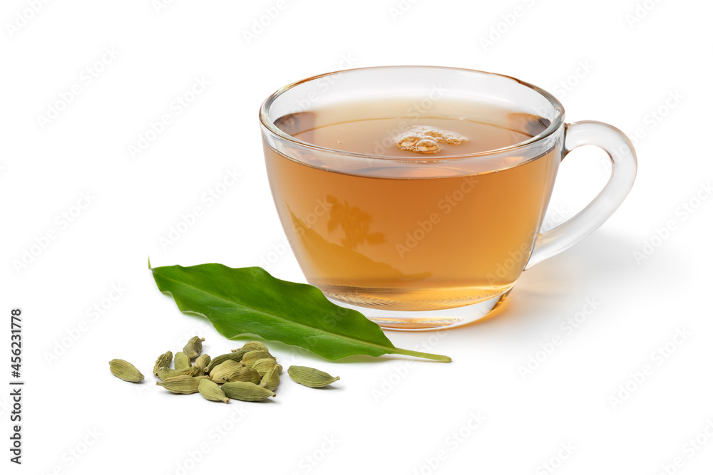 Glass cup with Cardamom tea and a heap with cardamom seeds and leaf in front isolated on white background Glass cup with Cardamom tea and a heap with cardamom seeds and leaf in front isolated on white background