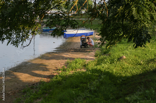 Man walking with the baby carriage on the river shore in front of the boats. © Daria