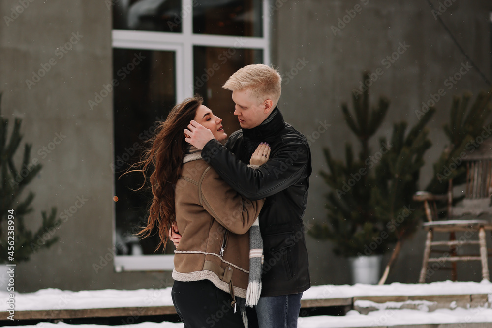 A man and a woman in love in winter clothes hug and warm themselves standing on the snowy terrace of a country house in cold weather on Christmas weekend, a selective focus A man and a woman in love in winter clothes hug and warm themselves standing on the snowy terrace of a country house in cold weather on Christmas weekend, a selective focus