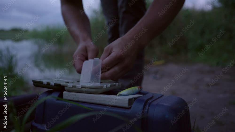 man fisherman tries to get tackle with his fingers from fishing box outdoors man fisherman tries to get tackle with his fingers from fishing box outdoors