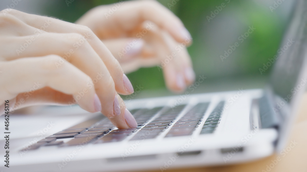 A freelance girl is typing a letter about work on the laptop keyboard. Close-up of a woman's fingers typing on a computer, against the background of a green garden on a sunny day. Work online.