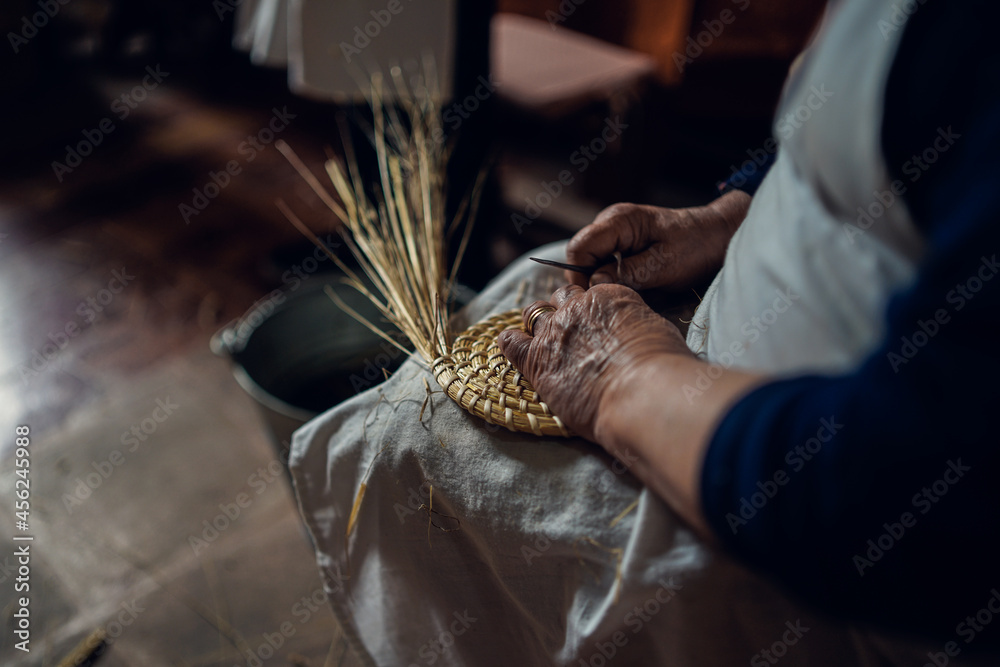 hands of an elderly woman working on ears of straws