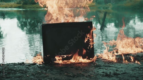 Retro vintage TV is burning with fire near the water. The water is also burning. Concept of post apocalypse, surrealism and the fire hazard of old worn out equipment