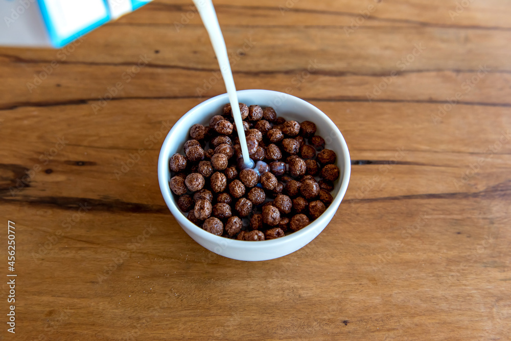 Pouring milk into chocolate cornflakes balls Breakfast with milk and cornflakes. Pouring milk into chocolate cornflakes balls Breakfast with milk and cornflakes.
