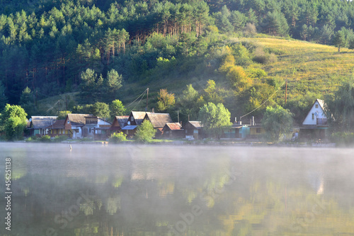 Waterfront houses by the misty lake. Between hills at summer dawn. Arló, Hungary