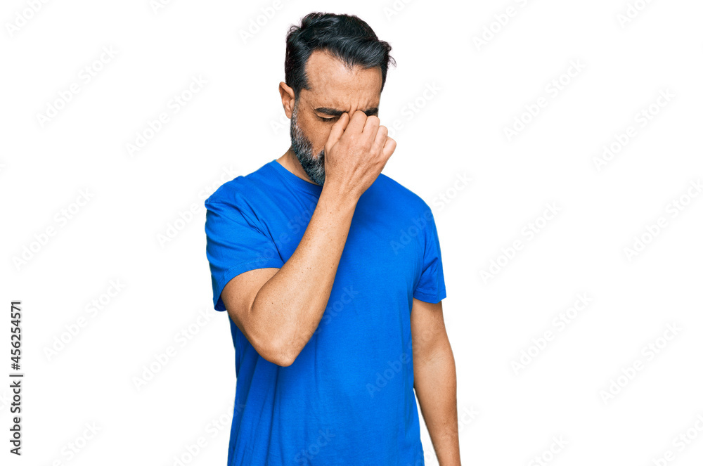 Middle aged man with beard wearing casual blue t shirt tired rubbing nose and eyes feeling fatigue and headache. stress and frustration concept. Middle aged man with beard wearing casual blue t shirt tired rubbing nose and eyes feeling fatigue and headache. stress and frustration concept.