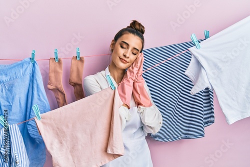 Beautiful brunette young woman washing clothes at clothesline sleeping tired dreaming and posing with hands together while smiling with closed eyes.