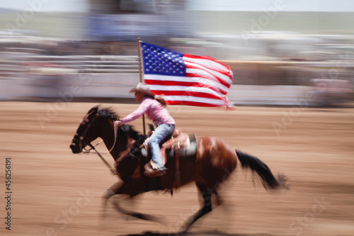 Cowgirl rides in rodeo with American flag. Motion blur Galisteo, New Mexico, United States. photo