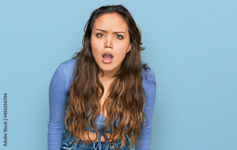 Young hispanic girl wearing casual clothes in shock face, looking skeptical and sarcastic, surprised with open mouth Young hispanic girl wearing casual clothes in shock face, looking skeptical and sarcastic, surprised with open mouth