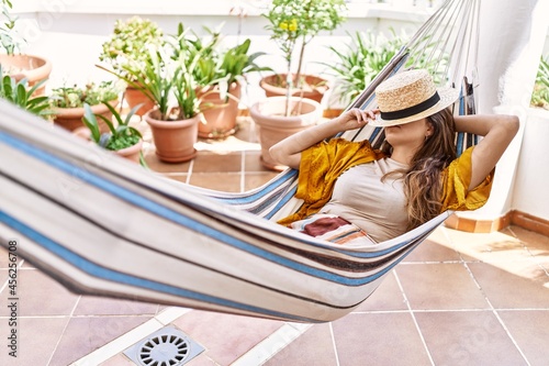 Young hispanic girl covering face with hat sleeping on hammock at the terrace.