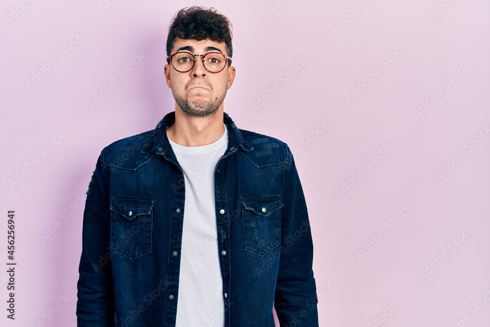 Young hispanic man wearing casual clothes and glasses puffing cheeks with funny face. mouth inflated with air, crazy expression. Young hispanic man wearing casual clothes and glasses puffing cheeks with funny face. mouth inflated with air, crazy expression.