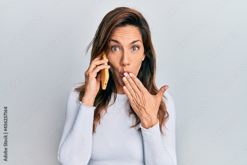 Young latin woman having conversation talking on the smartphone covering mouth with hand, shocked and afraid for mistake. surprised expression Young latin woman having conversation talking on the smartphone covering mouth with hand, shocked and afraid for mistake. surprised expression
