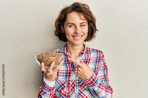 Young brunette woman holding bowl with lentils smiling happy pointing with hand and finger
