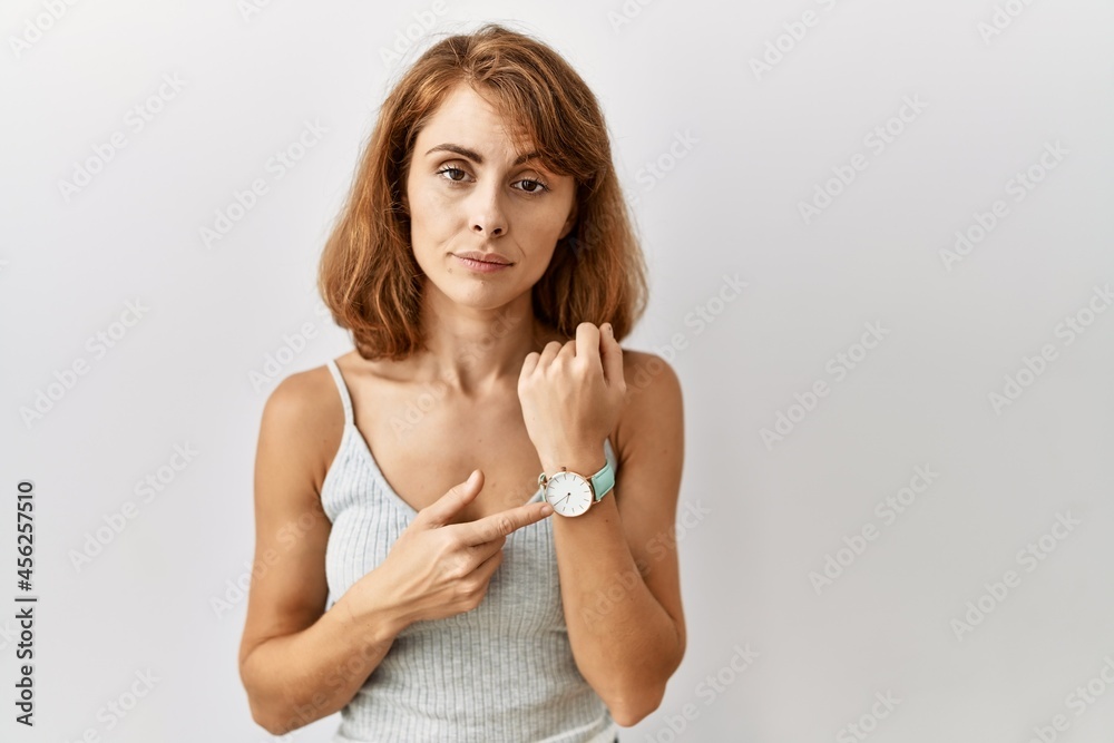 Beautiful caucasian woman standing over isolated background in hurry pointing to watch time, impatience, looking at the camera with relaxed expression