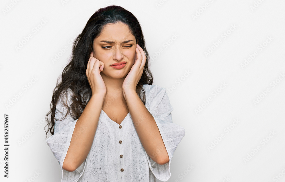 Brunette young woman wearing casual clothes covering ears with fingers with annoyed expression for the noise of loud music. deaf concept. Brunette young woman wearing casual clothes covering ears with fingers with annoyed expression for the noise of loud music. deaf concept.