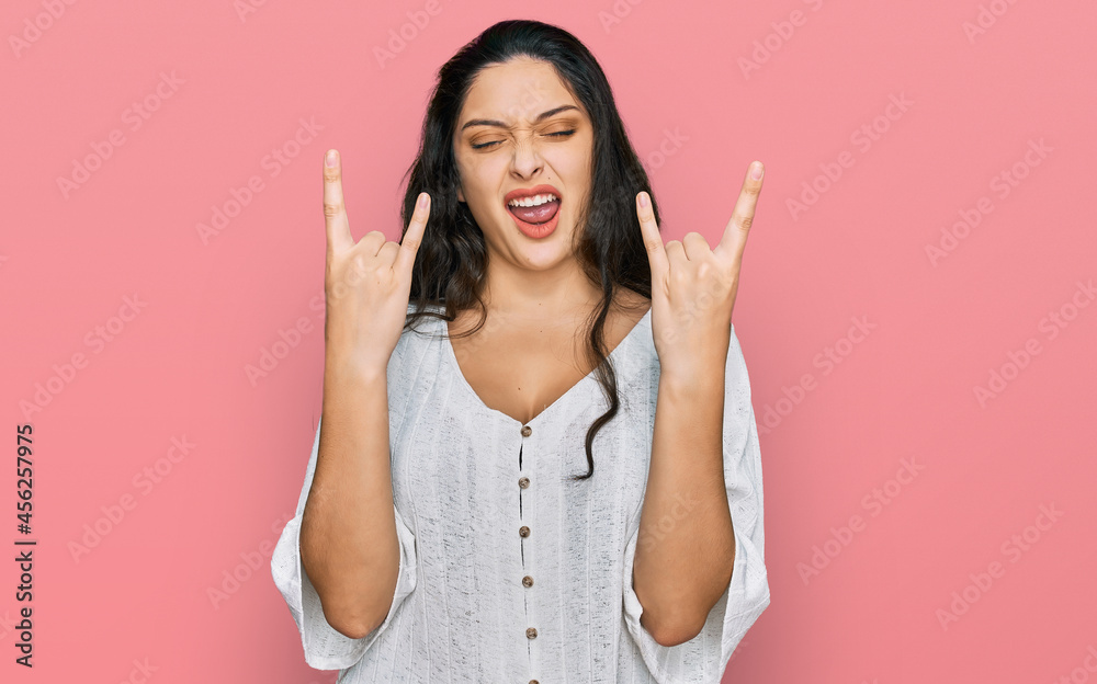 Brunette young woman wearing casual clothes shouting with crazy expression doing rock symbol with hands up. music star. heavy concept. Brunette young woman wearing casual clothes shouting with crazy expression doing rock symbol with hands up. music star. heavy concept.