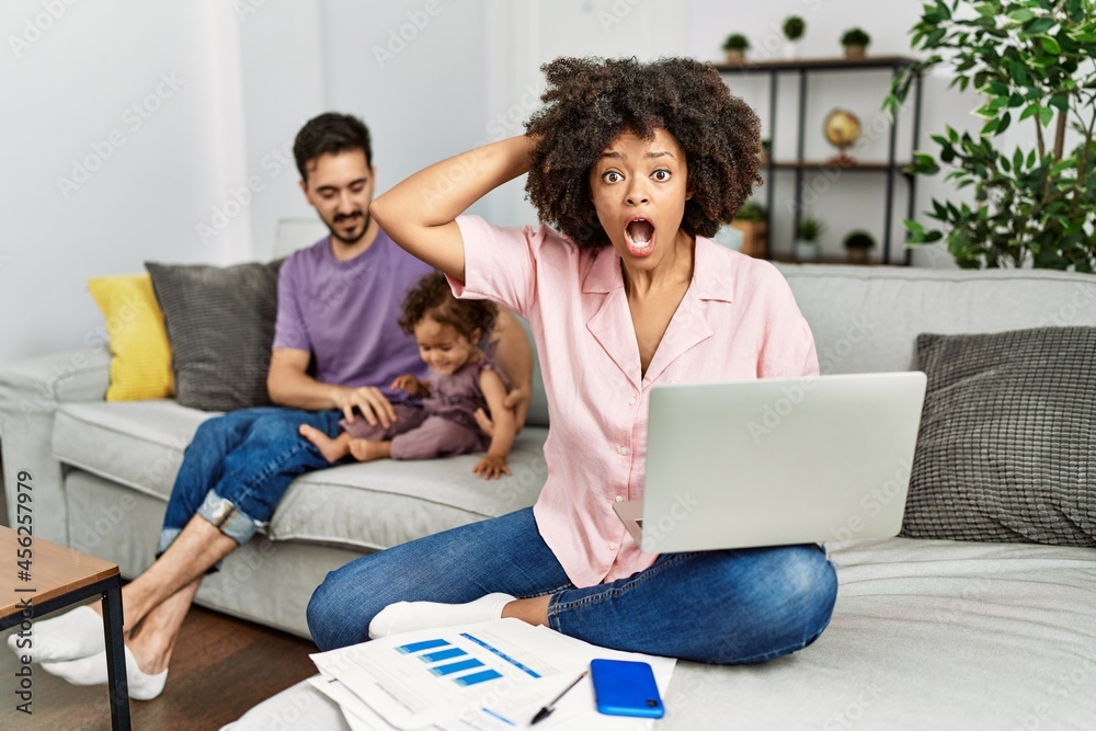 Mother of interracial family working using computer laptop at home crazy and scared with hands on head, afraid and surprised of shock with open mouth Mother of interracial family working using computer laptop at home crazy and scared with hands on head, afraid and surprised of shock with open mouth