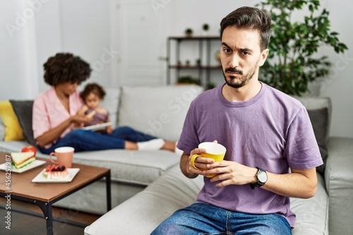 Hispanic father of interracial family drinking a cup coffee skeptic and nervous  frowning upset because of problem. negative person.
