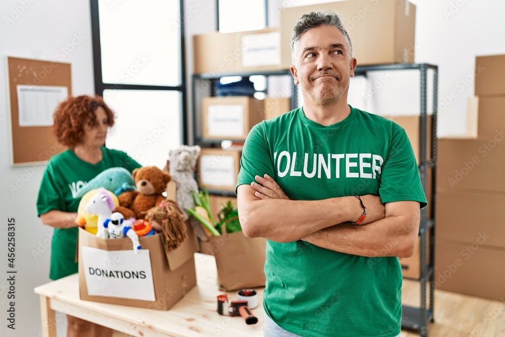 Middle age man wearing volunteer t shirt at donations stand smiling looking to the side and staring away thinking. Middle age man wearing volunteer t shirt at donations stand smiling looking to the side and staring away thinking.