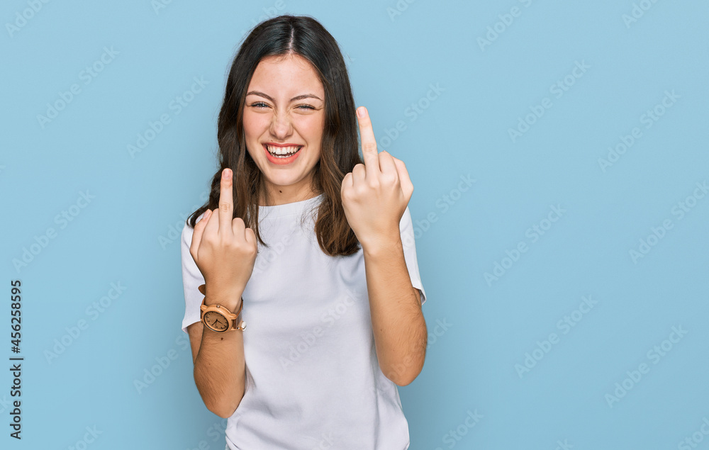 Young beautiful woman wearing casual white t shirt showing middle finger doing fuck you bad expression, provocation and rude attitude. screaming excited Young beautiful woman wearing casual white t shirt showing middle finger doing fuck you bad expression, provocation and rude attitude. screaming excited
