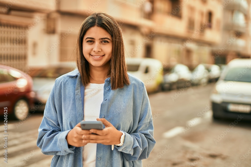 Young latin girl smiling happy using smartphone at the city.