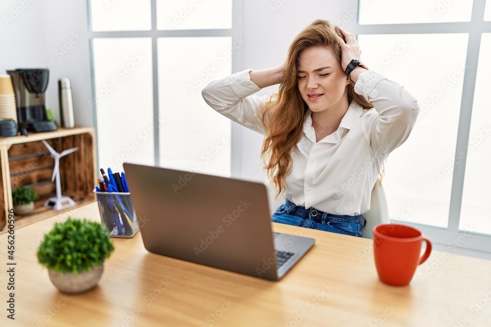Young caucasian woman working at the office using computer laptop suffering from headache desperate and stressed because pain and migraine. hands on head. Young caucasian woman working at the office using computer laptop suffering from headache desperate and stressed because pain and migraine. hands on head.