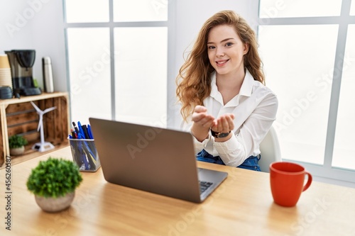 Young caucasian woman working at the office using computer laptop smiling with hands palms together receiving or giving gesture. hold and protection
