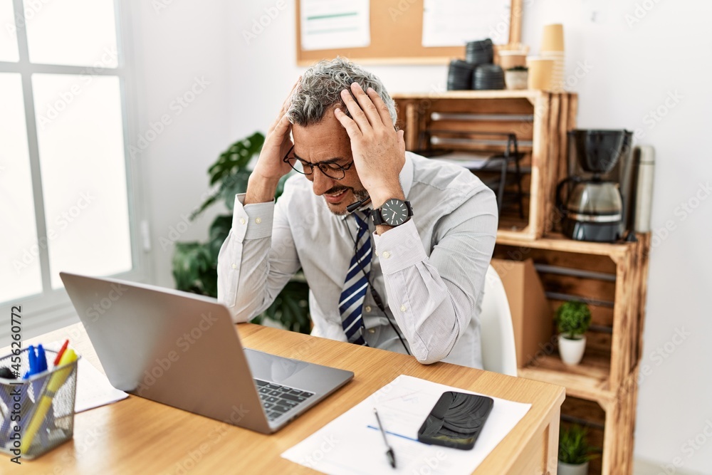 Middle age hispanic business man working at the office wearing operator headset suffering from headache desperate and stressed because pain and migraine. hands on head. Middle age hispanic business man working at the office wearing operator headset suffering from headache desperate and stressed because pain and migraine. hands on head.