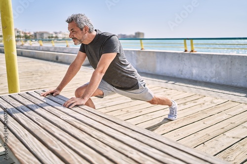 Middle age hispanic man wearing sportswear stretching at seaside