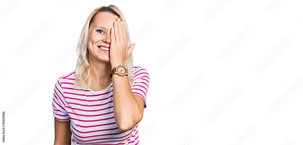 Young caucasian woman wearing casual clothes covering one eye with hand, confident smile on face and surprise emotion. Young caucasian woman wearing casual clothes covering one eye with hand, confident smile on face and surprise emotion.