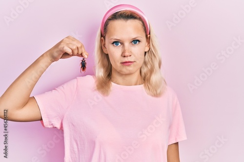 Obraz na plátně Beautiful caucasian blonde woman holding cockroach thinking attitude and sober e