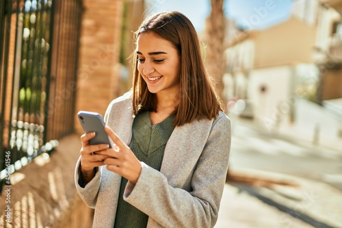 Young hispanic girl smiling happy using smartphone at the city.