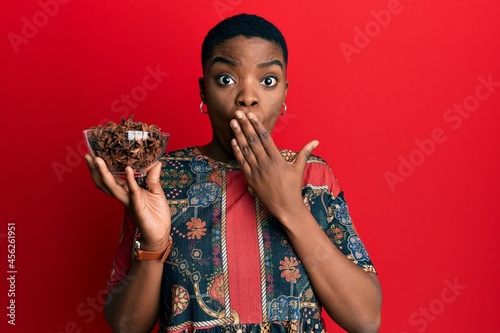 Young african american woman holding bowl of star anise covering mouth with hand  shocked and afraid for mistake. surprised expression