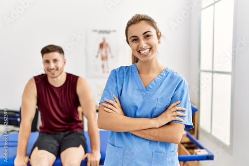 Young hispanic physioterapist woman smiling happy standing with arms crossed gesture at the clinic