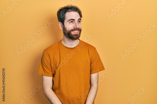 Caucasian man with beard wearing casual yellow t shirt smiling looking to the side and staring away thinking.