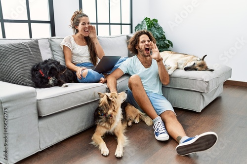 Photography Young hispanic couple with dogs relaxing at home shouting and screaming loud to side with hand on mouth