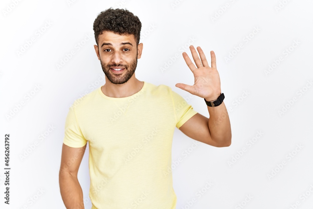 Arab young man standing over isolated background showing and pointing up with fingers number five while smiling confident and happy. Arab young man standing over isolated background showing and pointing up with fingers number five while smiling confident and happy.