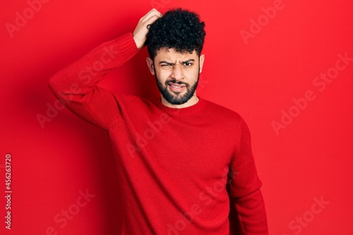Foto Young arab man with beard wearing casual red sweater confuse and wonder about question