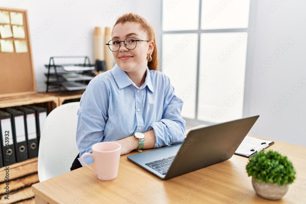 Young redhead woman working at the office using computer laptop smiling looking to the side and staring away thinking. Young redhead woman working at the office using computer laptop smiling looking to the side and staring away thinking.