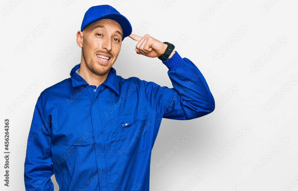 Bald man with beard wearing builder jumpsuit uniform smiling pointing to head with one finger, great idea or thought, good memory
