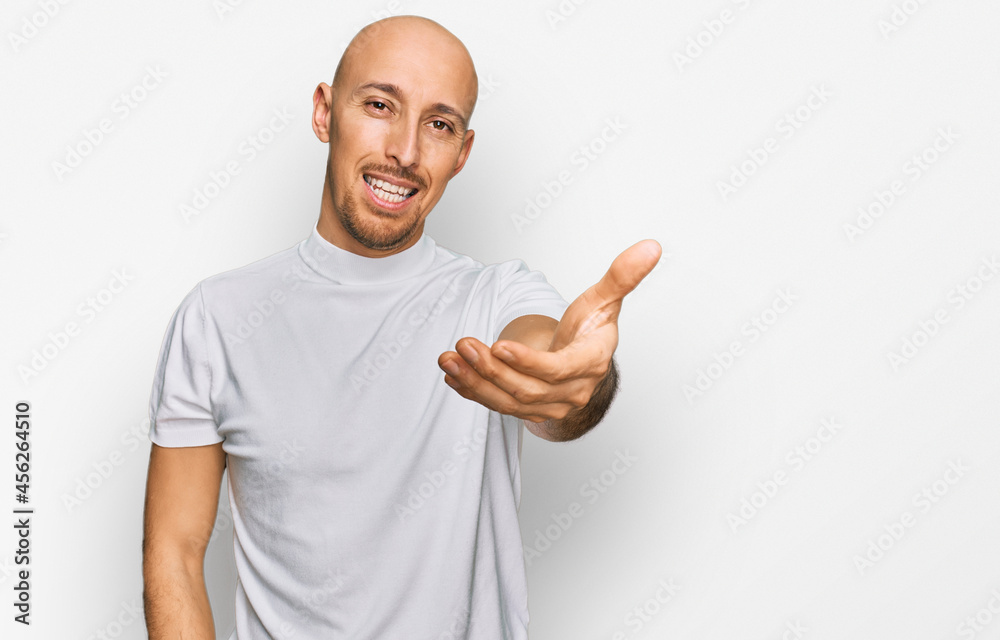 Bald man with beard wearing casual white t shirt smiling friendly offering handshake as greeting and welcoming. successful business. Bald man with beard wearing casual white t shirt smiling friendly offering handshake as greeting and welcoming. successful business.