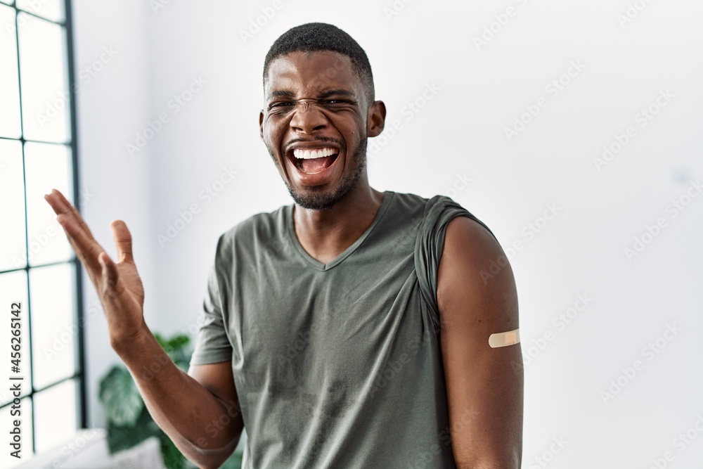 Young african american man getting vaccine showing arm with band aid screaming proud, celebrating victory and success very excited with raised arms Young african american man getting vaccine showing arm with band aid screaming proud, celebrating victory and success very excited with raised arms