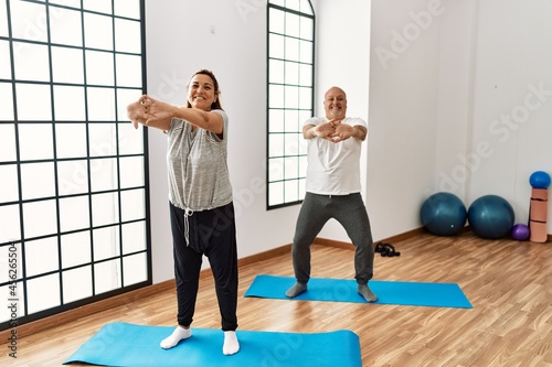 Middle age hispanic couple stretching at sport center.