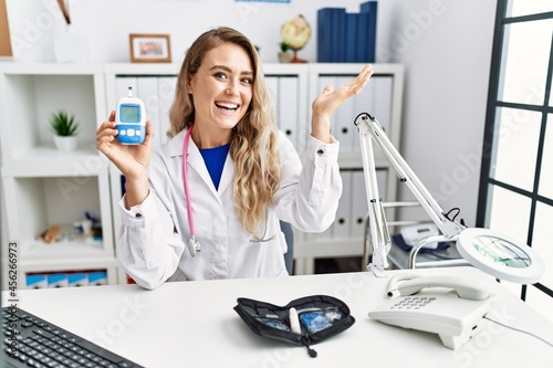 Young beautiful doctor woman holding glucose meter celebrating achievement with happy smile and winner expression with raised hand