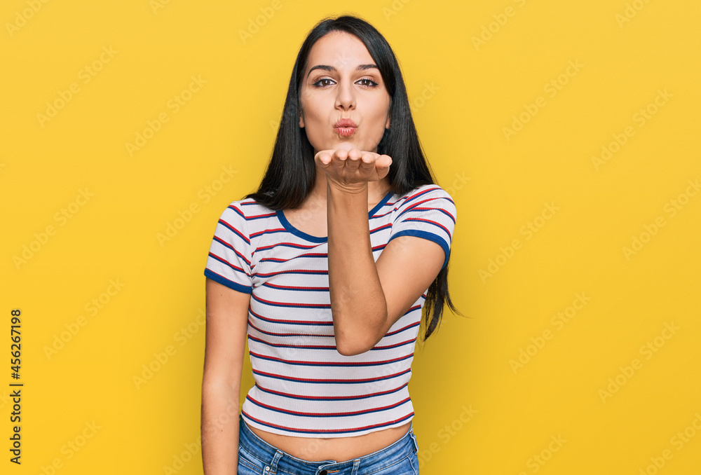 Young hispanic girl wearing casual striped t shirt looking at the camera blowing a kiss with hand on air being lovely and sexy. love expression. Young hispanic girl wearing casual striped t shirt looking at the camera blowing a kiss with hand on air being lovely and sexy. love expression.