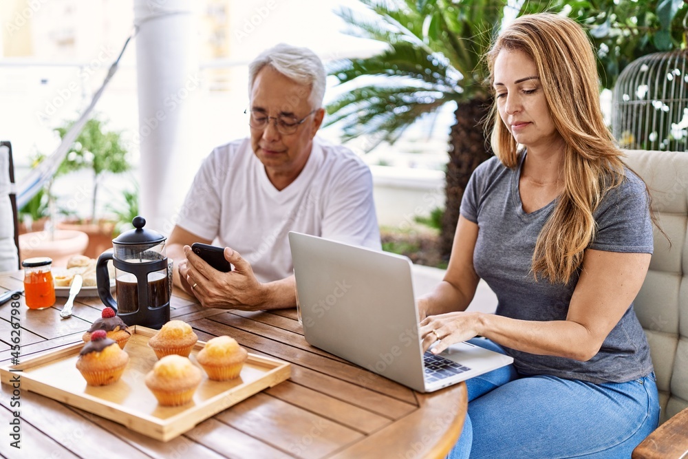 Middle age hispanic couple having breakfast using smartphone and laptop at the terrace. Middle age hispanic couple having breakfast using smartphone and laptop at the terrace.